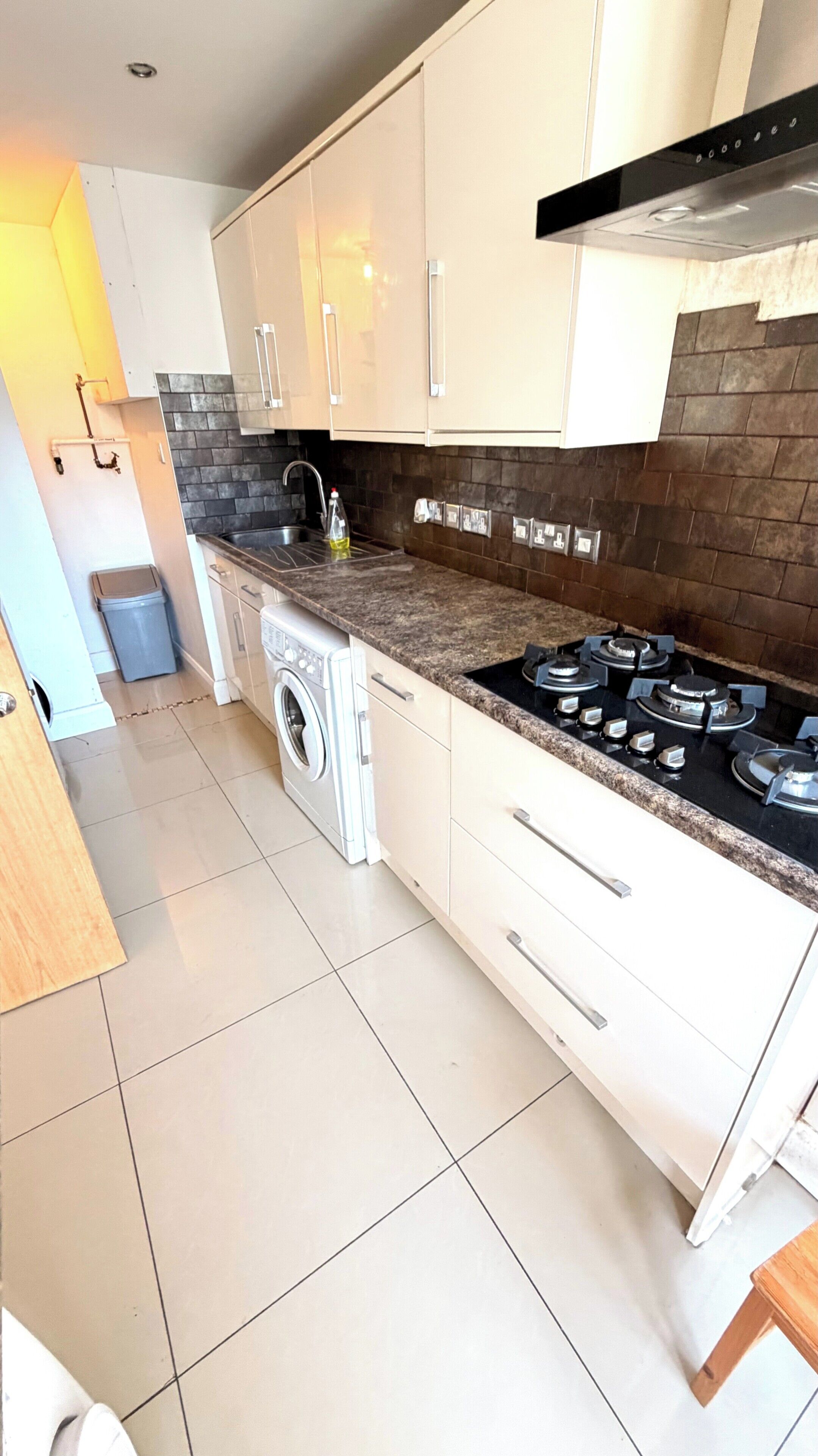 A modern kitchen with white cabinets, a built-in washing machine, a gas stove, and a tiled backsplash.