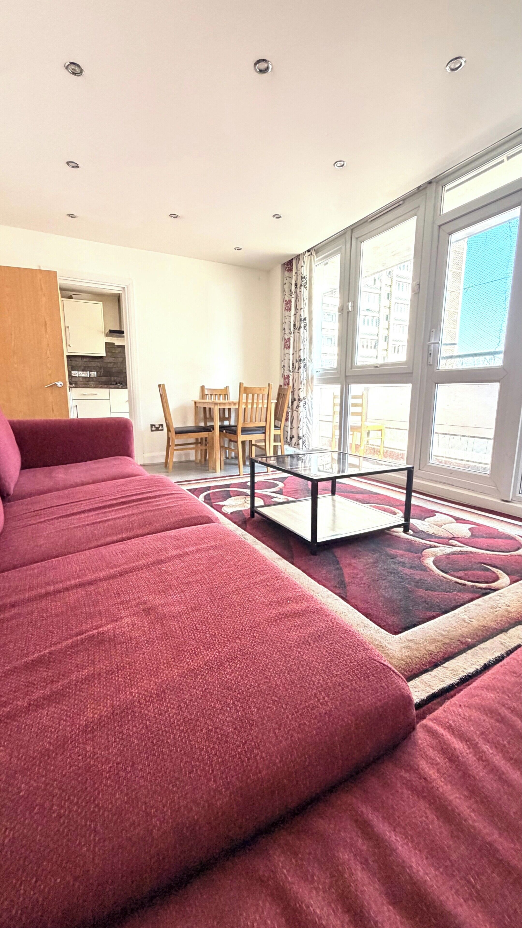 A bedroom with a large bed, a glass-top table, and a view of the city through large windows.