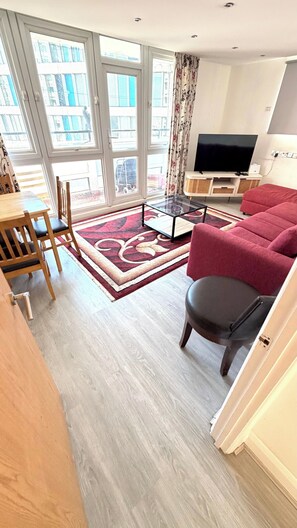A modern living room with a sofa, a TV, and a dining area with chairs and a table. - Luxury 4-bed Apartment Tower Paddington London (London)