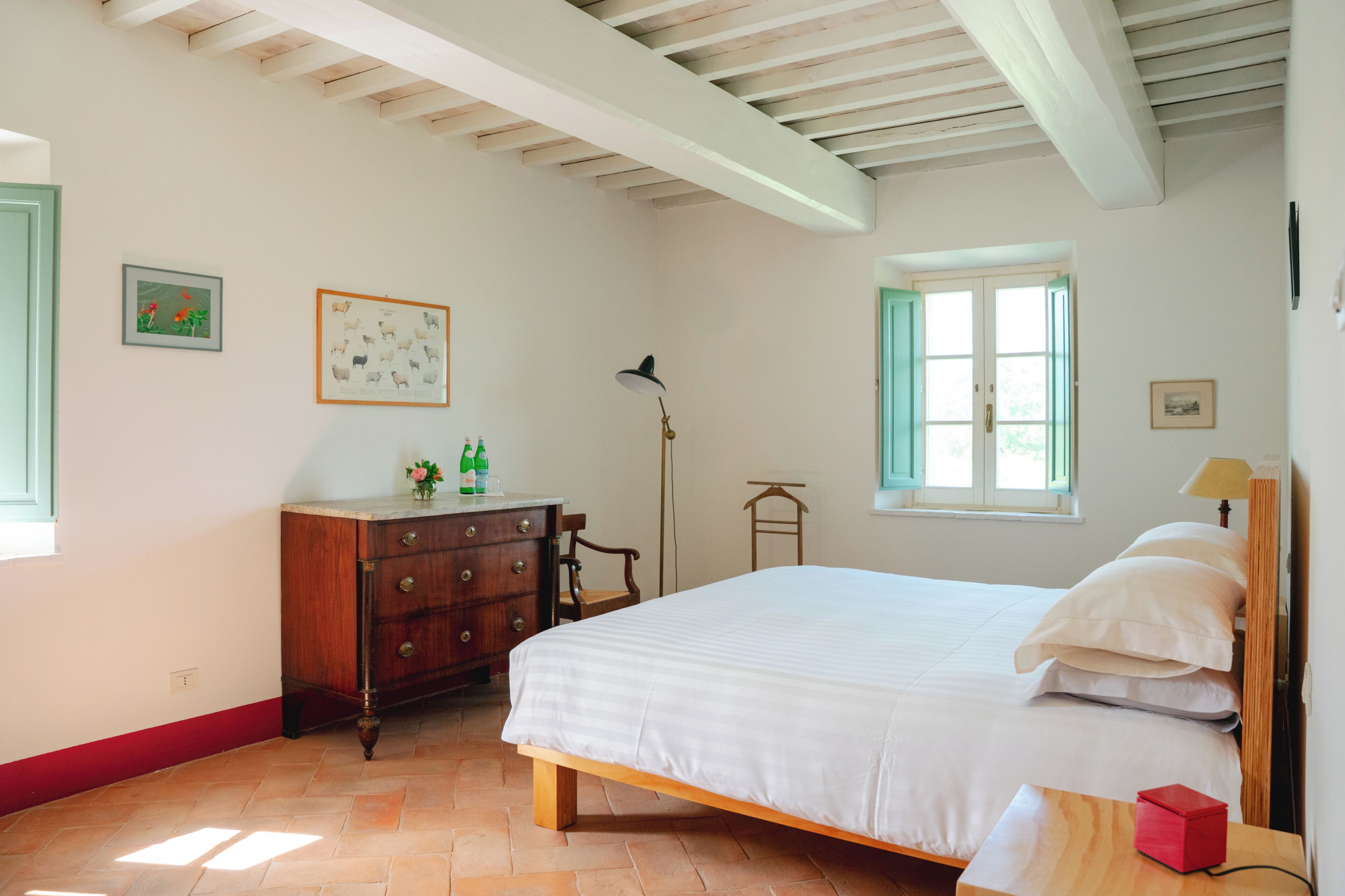 Ein Schlafzimmer mit Bett, Kommode, Lampe, Fenster und Kunstwerken.