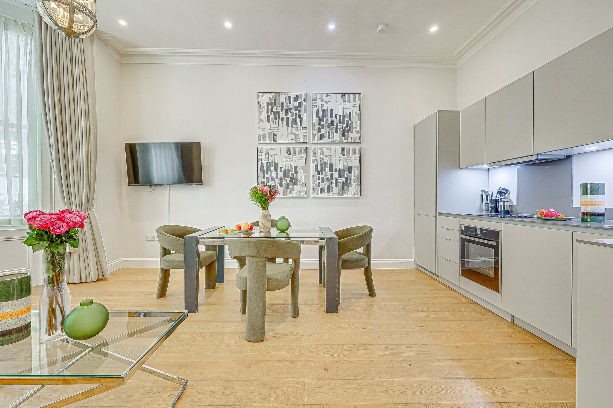 A modern kitchen with a dining area, a flat-screen TV, and a vase with flowers.