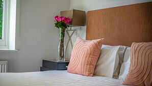 Una cama bien hecha con almohadas, una mesita de noche con una lámpara y un jarrón con flores.