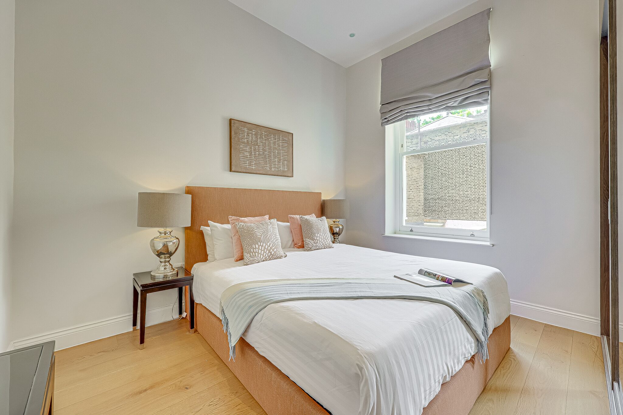 A bedroom with a bed, bedside tables, a window with curtains, and a wall-mounted artwork.