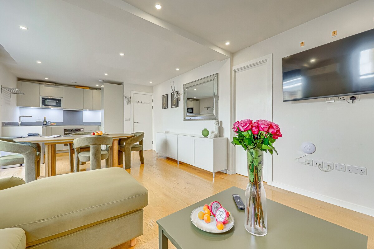 Una sala de estar moderna con comedor, cocina y televisor montado en la pared.