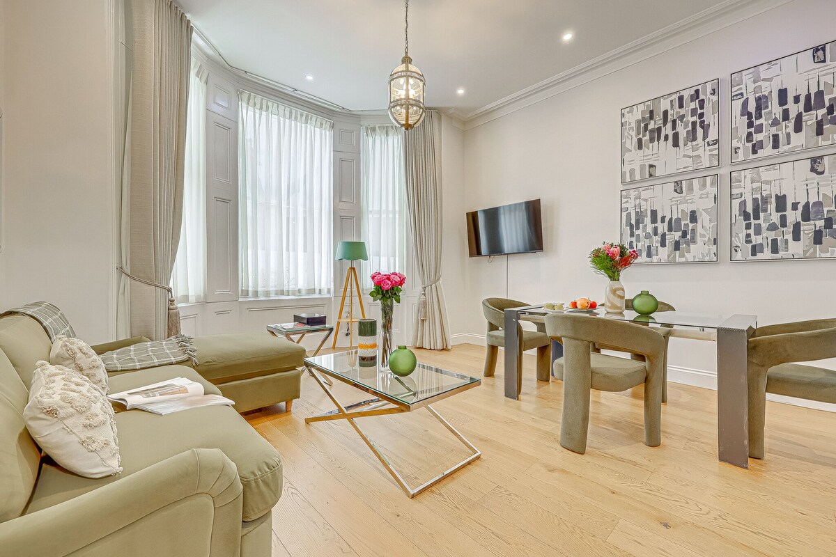 Una sala de estar moderna con un sofá, una mesa de centro de cristal, una mesa de comedor con sillas, un televisor montado en la pared y obras de arte.
