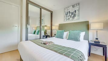 A hotel room with a large bed, a bedside table with a lamp, a mirror, and a wall-mounted artwork.