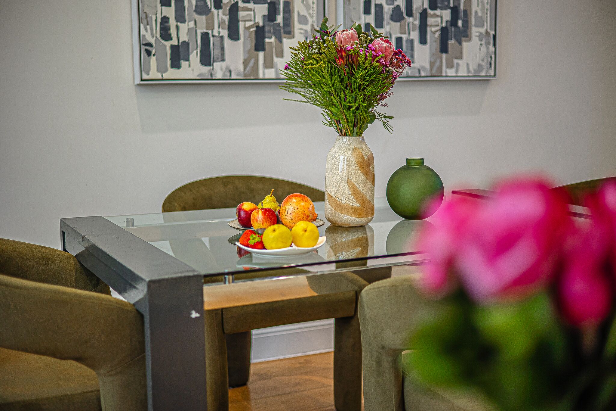 Un tavolo da pranzo con piano in vetro, circondato da sedie, e un vaso con fiori sopra.