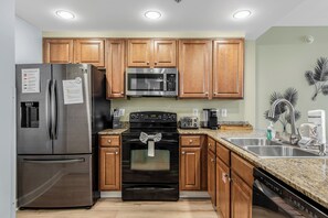A modern kitchen with stainless steel appliances, wooden cabinets, granite countertops, and a built-in oven. - 2 Oceanfront Masters + Bunk, Sleeps 10, PCB (Panama City Beach)
