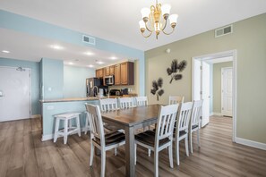 A modern kitchen with wooden cabinets, a central island, and a dining area with a wooden table and white chairs. - 2 Oceanfront Masters + Bunk, Sleeps 10, PCB (Panama City Beach)