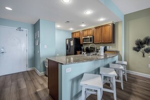 A modern kitchen with granite countertops, wooden cabinets, and a built-in microwave. - 2 Oceanfront Masters + Bunk, Sleeps 10, PCB (Panama City Beach)