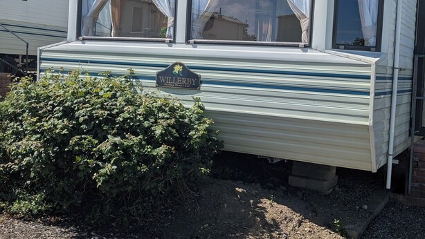 Una caravana con el rótulo 'WILLERBY Holiday Homes Ltd', ventanas grandes con cortinas y un pequeño jardín.