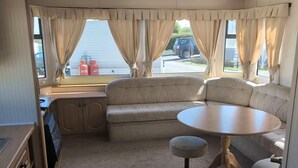 Interior compacto de autocaravana con kitchenette, zona de estar acolchada y una pequeña mesa redonda.