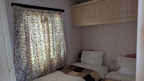 Una habitación pequeña con una cama individual, una cortina, una colcha estampada y un armario de madera.