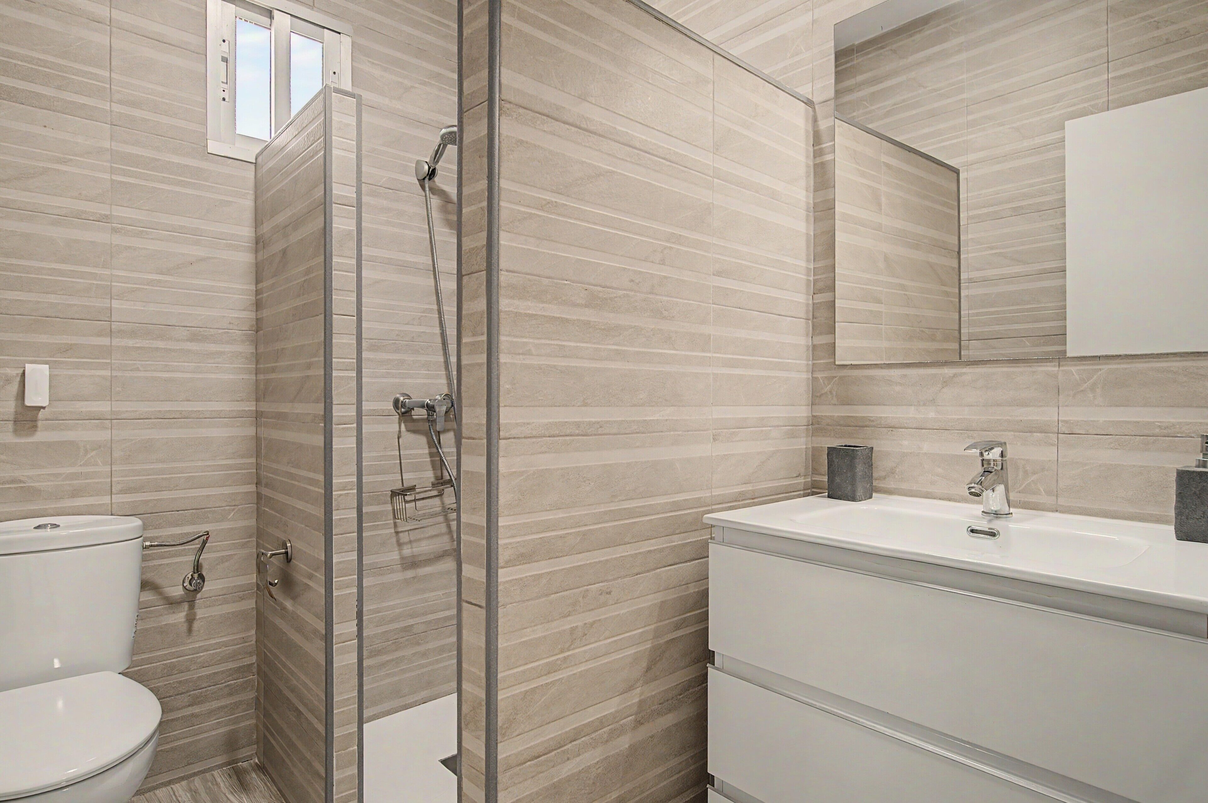 A modern bathroom with a glass shower enclosure, a toilet, and a sink with a mirror above.