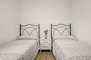 Ein Doppelzimmer mit zwei Betten, jeweils mit Kopfteil, einem Nachttisch mit Vase und einer Schublade.