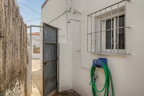 Ein schmaler Gang mit einem Metallgitter, einem vergitterten Fenster und einem an der Wand befestigten Schlauch.