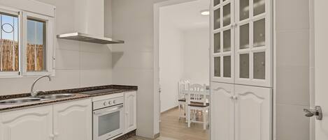 A modern kitchen with white cabinetry, a granite countertop, a stainless steel range hood, and a dining area with a table and chairs.