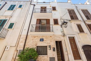 A multi-story building with balconies, a stone facade, and a blue sign indicating the address. - Helios Home (Conversano)