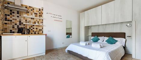 Un dormitorio con cama, kitchenette, salpicadero de azulejos y espejo montado en la pared.