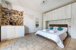 Um quarto com cama, bancada de cozinha compacta, painel de azulejos e espelho fixado na parede.