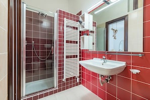 Un baño con cabina de ducha de vidrio, lavamanos blanco y paredes de azulejos rojos.