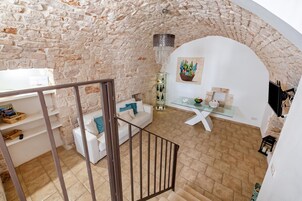 Um quarto com parede de pedra, um sofá branco, uma mesa de vidro com um vaso e uma escada.