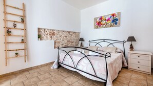 Ein Schlafzimmer mit einem Bett, Nachttisch, Lampe und einem an der Wand befestigten Regal mit Pflanzen.