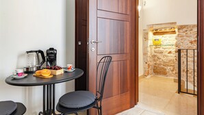 Ein kompakter Raum mit Holztür, einem kleinen Tisch mit Wasserkocher, Kaffeemaschine und Obstkorb.
