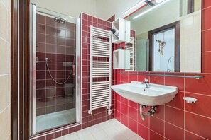 A modern bathroom with a glass shower enclosure, a white sink, and a red-tiled wall. - Helios Home (Conversano)