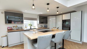 A modern kitchen with a central island, bar stools, and pendant lighting. - Corner Cottage in Malpas Cheshire (Malpas)