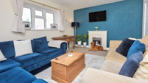 A living room with a blue sofa, a wooden coffee table, and a fireplace. - Corner Cottage in Malpas Cheshire (Malpas)