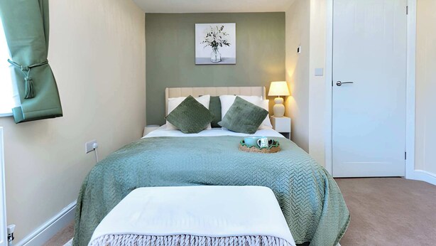 A bedroom with a bed, pillows, a bedside lamp, a door, and a wall-mounted artwork. - Corner Cottage in Malpas Cheshire (Malpas)