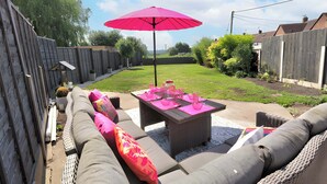 An outdoor patio with a sofa set, a table with pink placemats, and a red umbrella. - Corner Cottage in Malpas Cheshire (Malpas)