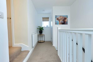 Um corredor com piso coberto por carpete, corrimão branco, planta em vaso e um quadro de um touro na parede.