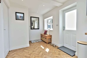 Ein Flur mit Holzboden, einem Spiegel, einem gerahmten Bild, einer Holzbank und einer Tür mit Fußmatte.
