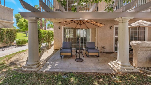A covered patio with two chairs and a table, columns, and a pergola. - Mesquite Breeze - A Ryson Property (Palm Springs)