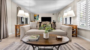 A living room with a sofa, coffee table, lamps, a TV, and a plant. - Mesquite Breeze - A Ryson Property (Palm Springs)