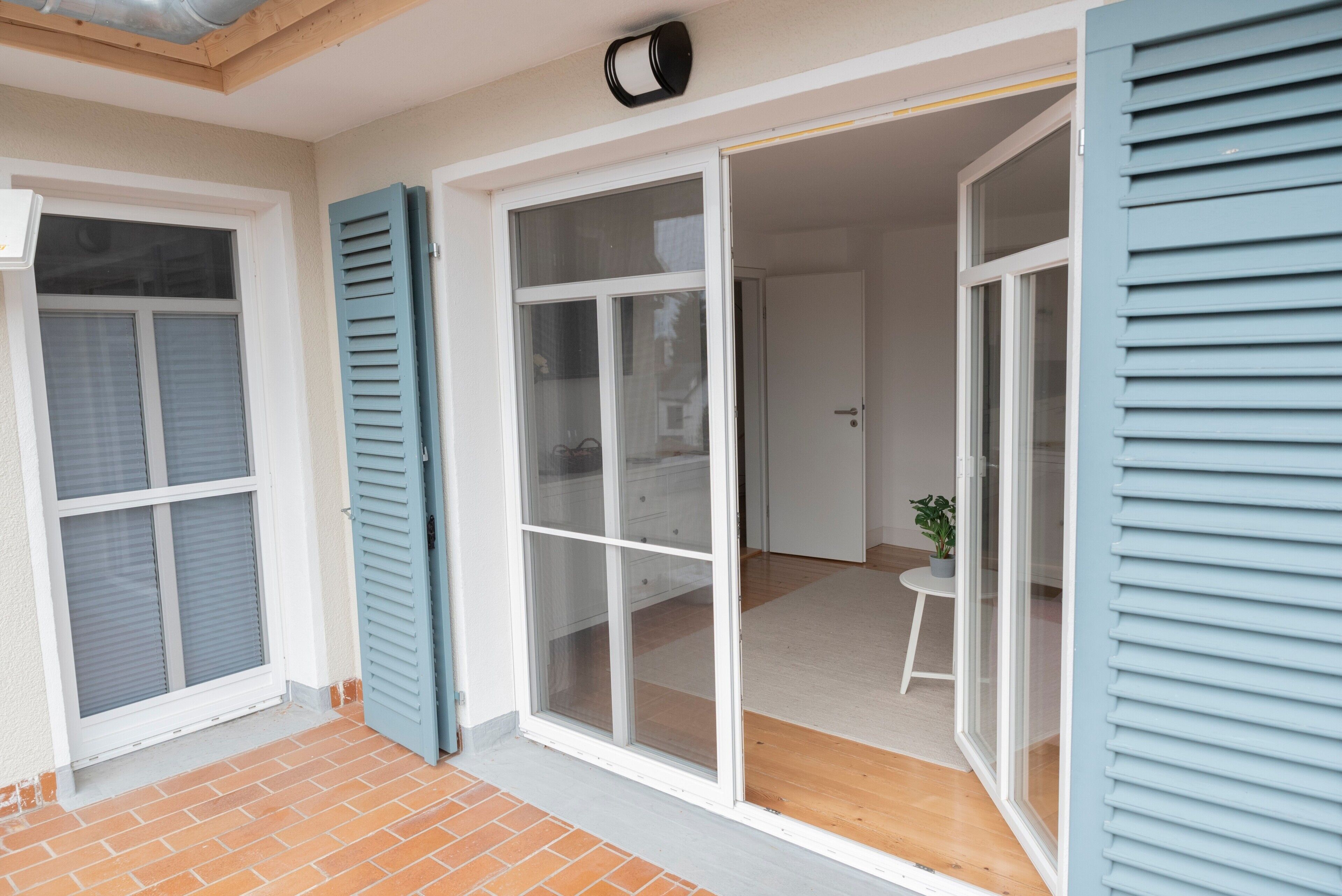 A room with a sliding glass door, a small table with a plant, and a white door leading to another room.
