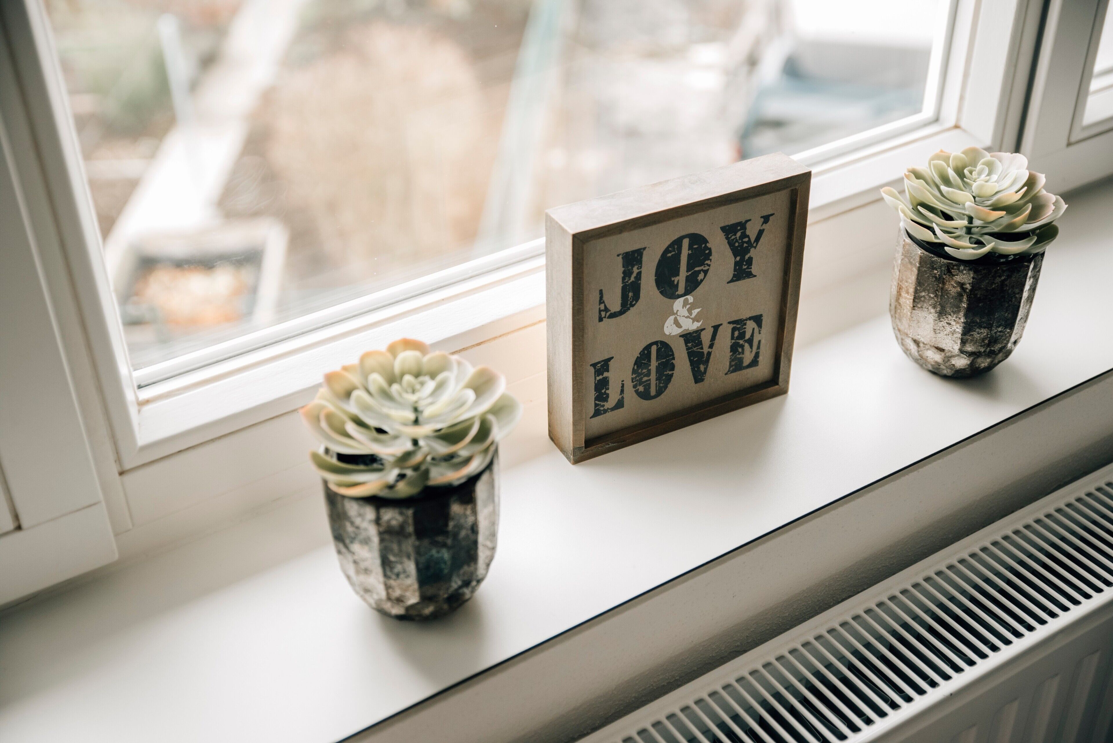 En vindueskarm med to krukker med sukkulenter og et billede med teksten 'JOY & LOVE'.