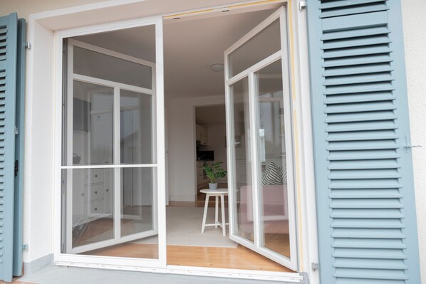 A room with a sliding glass door, a small table with a plant, and a glimpse of a kitchen area.