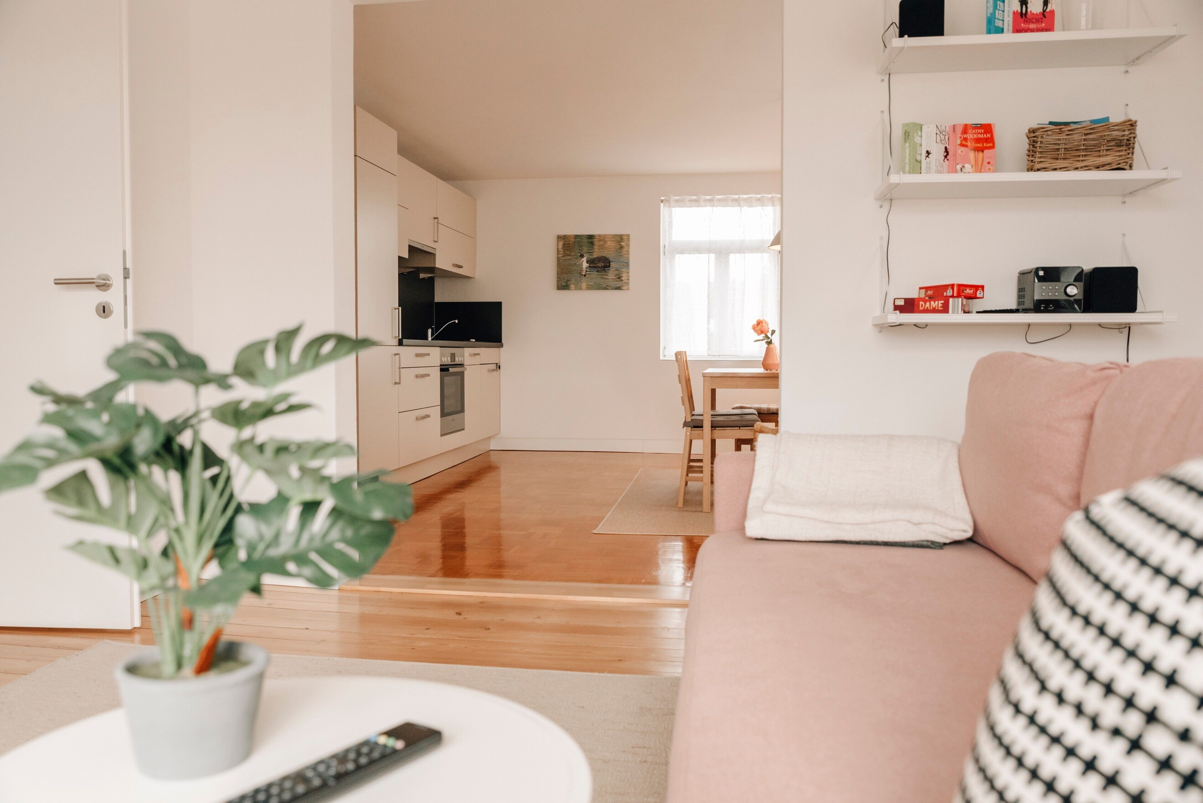Un salon moderne comprenant un canapé, une table basse avec une télécommande, une plante en pot et un coin repas avec une table et des chaises.