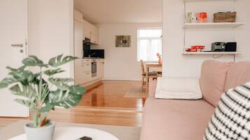 Un salon moderne comprenant un canapé, une table basse avec une télécommande, une plante en pot et un coin repas avec une table et des chaises.