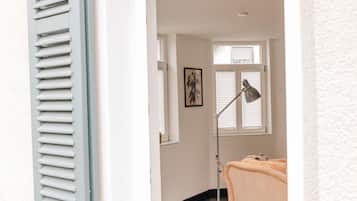 Ein Zimmer mit einem Bett, einer Stehlampe, einem gerahmten Bild an der Wand und einem Fenster mit Jalousien.