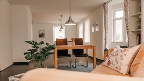 A modern living room with a sofa, a dining table with chairs, a hanging light fixture, and a potted plant. - Apartment 'Ferienwohnung Ambiente Am Federsee' with Wi-Fi (Bad Buchau)