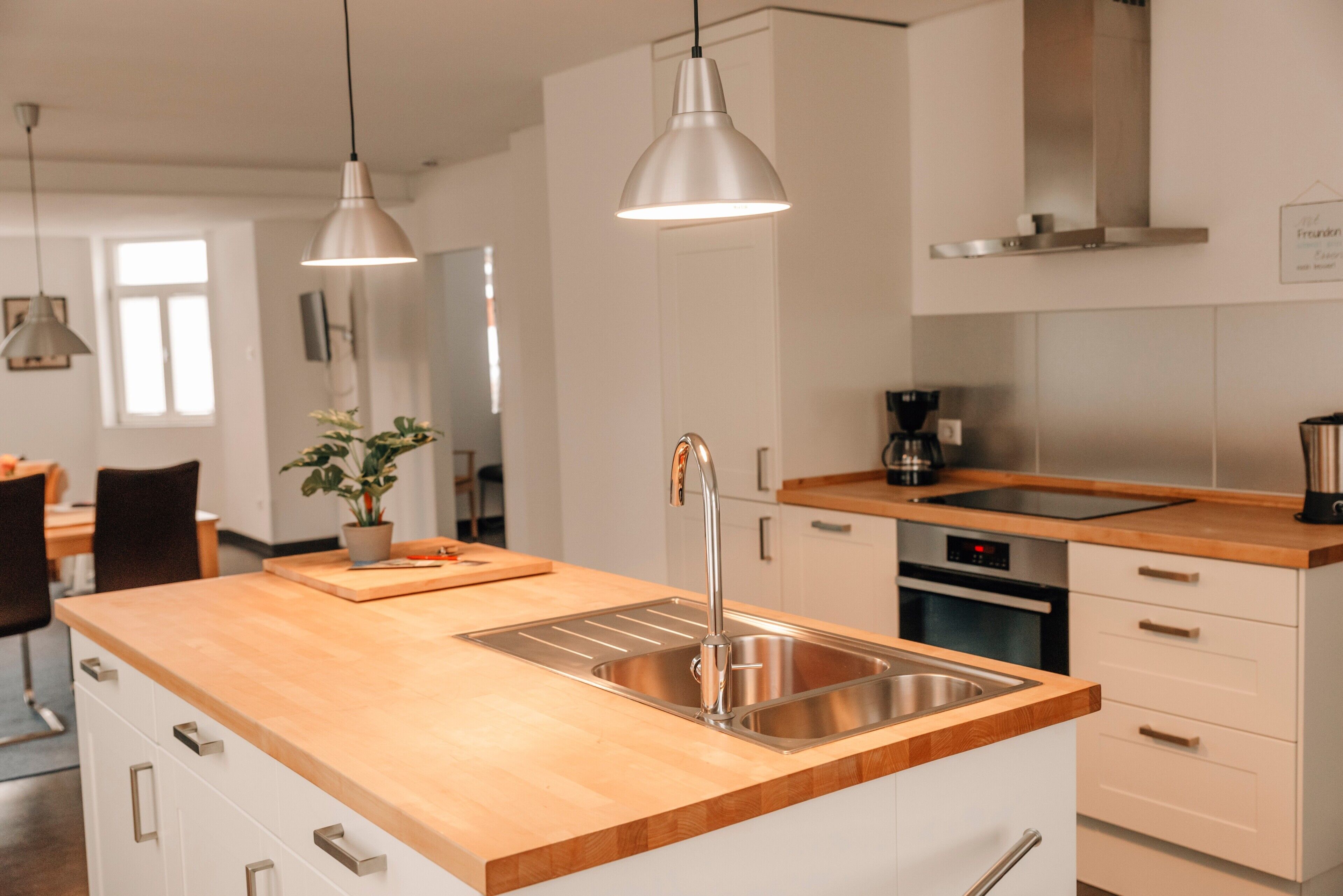 Une cuisine moderne dotée d’un plan de travail en bois, d’un évier en acier inoxydable et de luminaires suspendus.