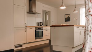 A modern kitchen with white cabinetry, a built-in oven, a stainless steel range hood, and pendant lighting. - Apartment 'Ferienwohnung Ambiente Am Federsee' with Wi-Fi (Bad Buchau)