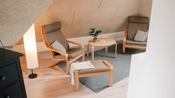 Ein modernes Schlafzimmer im Loft-Stil mit schrägem Dach, einem Holztisch, zwei Sesseln, einem kleinen Tisch und einer Stehlampe.