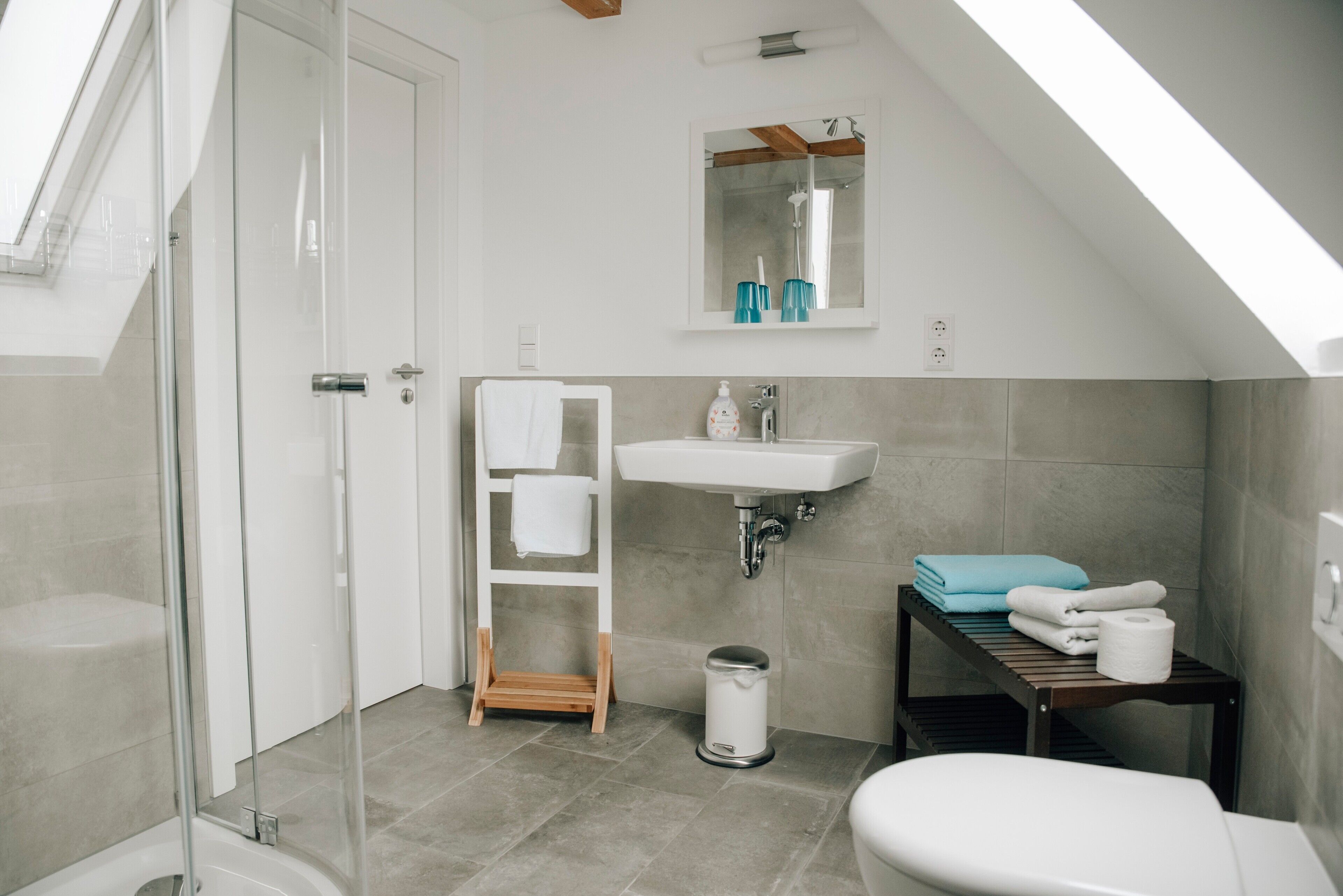 Ein modernes Badezimmer mit Dusche, Toilette, Waschbecken und einer kleinen Holzablage mit Handtüchern.