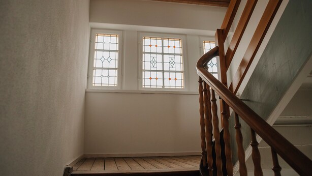 Un escalier avec des balustrades en bois menant à un palier doté de trois fenêtres.
