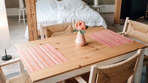 Une table à manger en bois, ornée d’un vase contenant une seule rose, de deux sets de table à rayures et de chaises en osier.